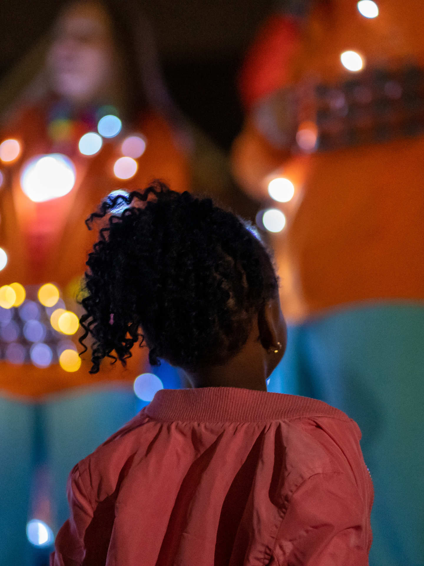 Image of small child in red jacket watching musicians with fairy lights in the background